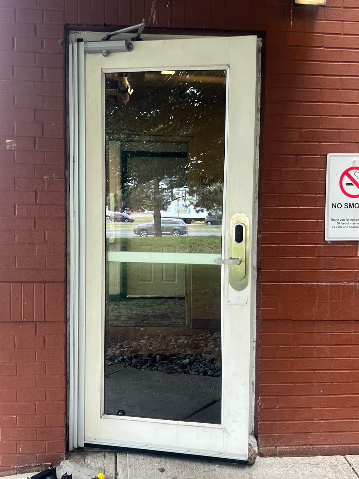 Aluminum-framed commercial storefront glass entry door with overhead closer and keypad lock on a red-brick Paterson, NJ building, serviced by Precision Windows & Glass