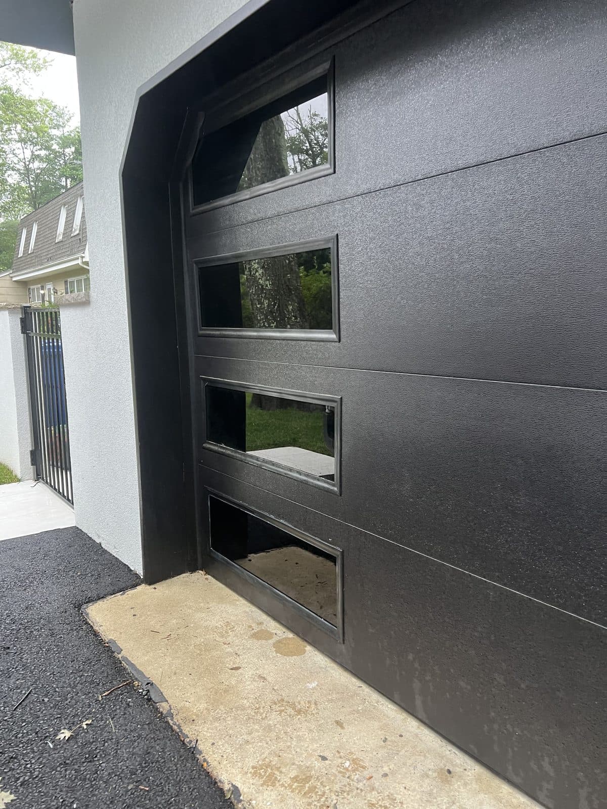 Contemporary flush black door with a stacked column of four rectangular glass vision lites on a modern stucco Garfield, NJ home, by Precision Windows & Glass